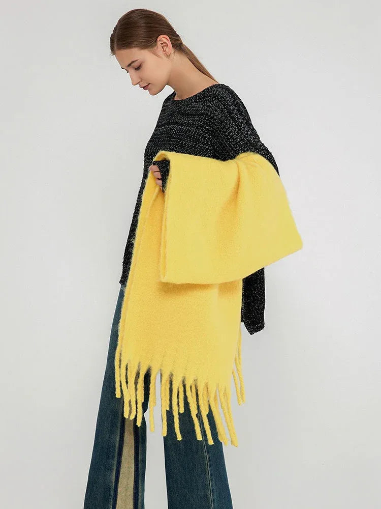 Woman holding a folded bright yellow scarf with prominent fringes.