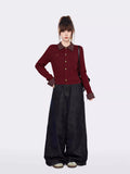 Full body shot of a woman in a burgundy cable knit cardigan and wide-leg jeans, standing against a white background.