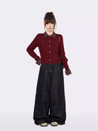 Full body shot of a woman in a burgundy cable knit cardigan and wide-leg jeans, standing against a white background.