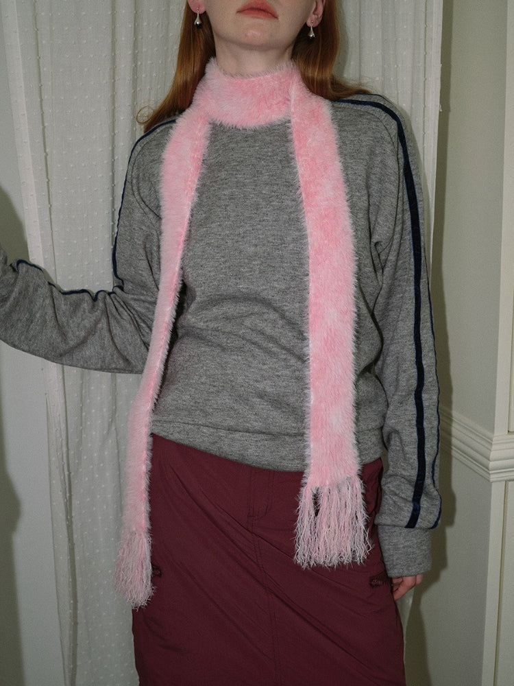 Woman from the chest up wearing a gray sweatshirt and a pink fuzzy scarf with fringed ends.
