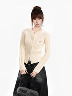 Close-up of a woman wearing a cream cable knit cropped cardigan with a crew neck and button front, showcasing the embroidered logo detail.