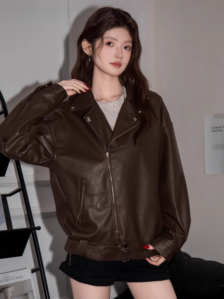 Front view of a woman in a brown faux leather moto jacket, showcasing the zippered pockets.