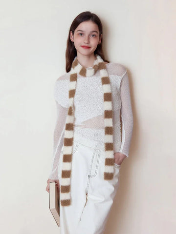 Woman wearing a white long-sleeved top and white pants, accessorized with a brown and white striped fuzzy scarf.