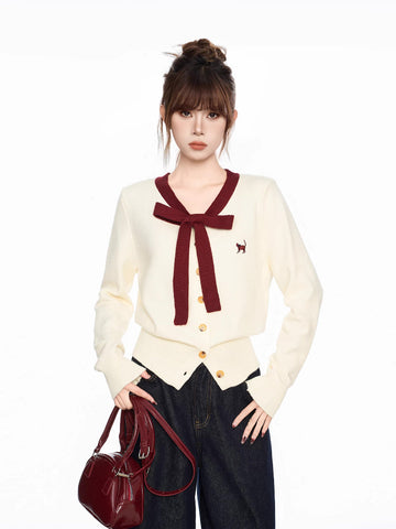 Cream knit cardigan with maroon trim and bow, featuring an embroidered cat detail and button closure.