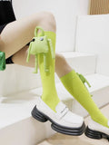 Lime green knee-high socks with a detachable plush frog toy on the left leg, worn with white loafers.