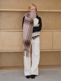 Model wearing a pink and brown plaid scarf with fringe detail.