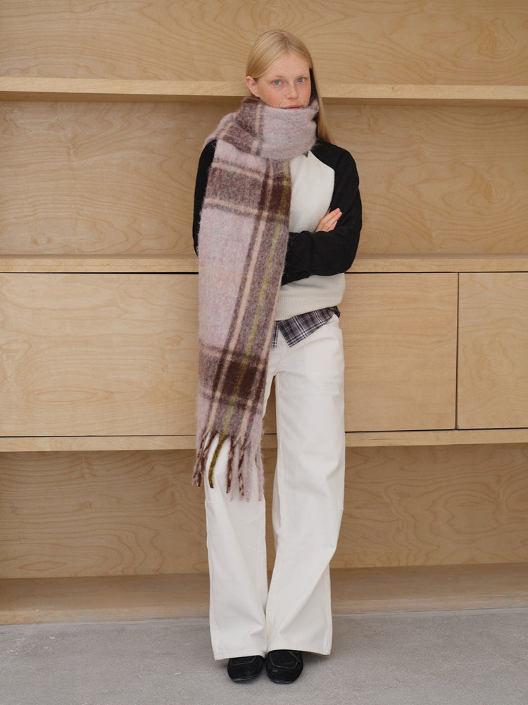 Model wearing a pink and brown plaid scarf with fringe detail.