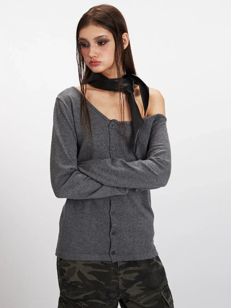 Model posing in a grey knit cardigan with an asymmetrical neckline and a black scarf.