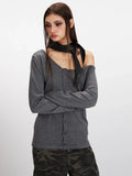 Model posing in a grey knit cardigan with an asymmetrical neckline and a black scarf.