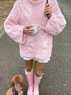 Woman holding a mug and umbrella in a pink chunky cable knit sweater
