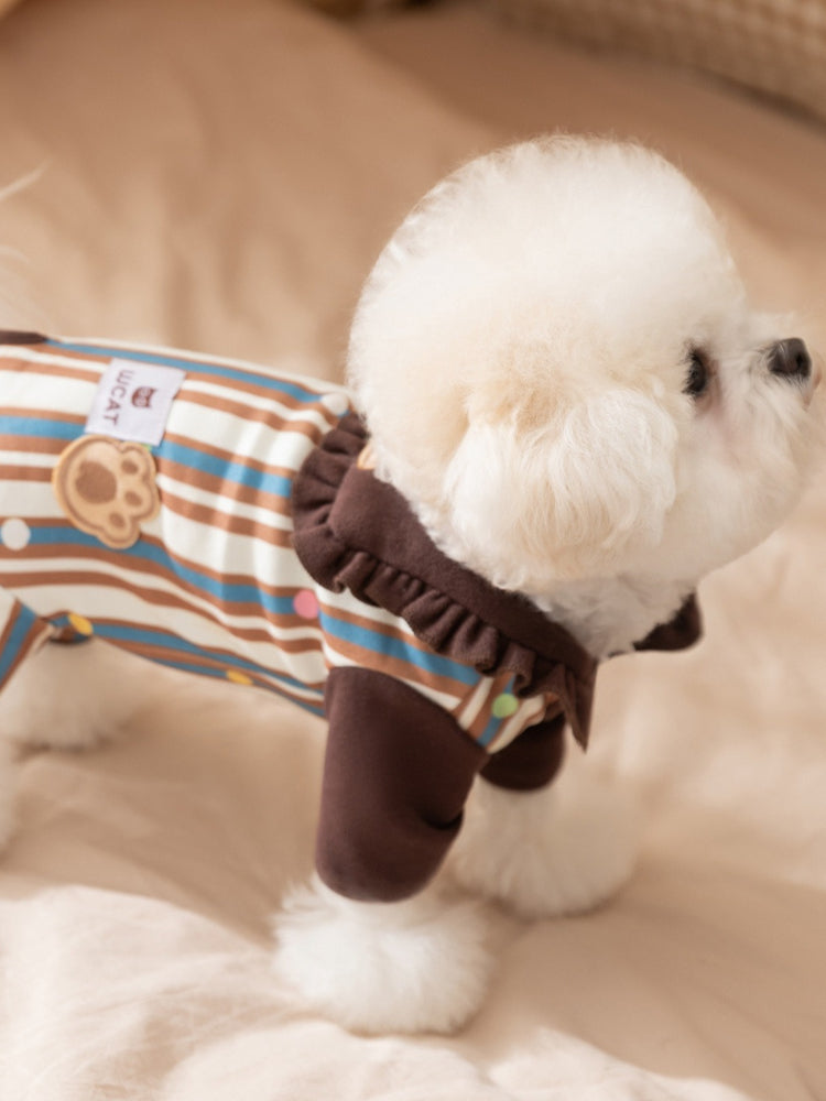 Profile view of a white dog wearing a brown and striped pet jumpsuit.