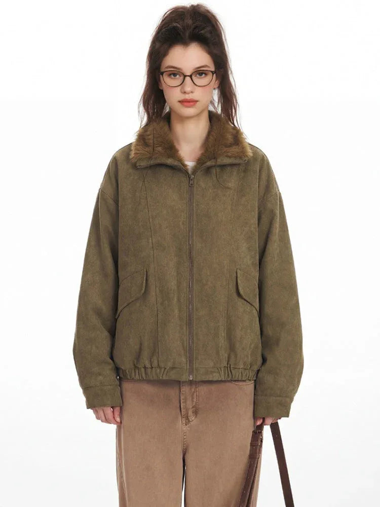 Front view of a woman in a green corduroy bomber jacket with a faux fur collar, tan pants, and glasses.