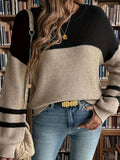 Front view of a woman in a color block knit sweater and blue jeans, accessorized with a gold necklace and belt.