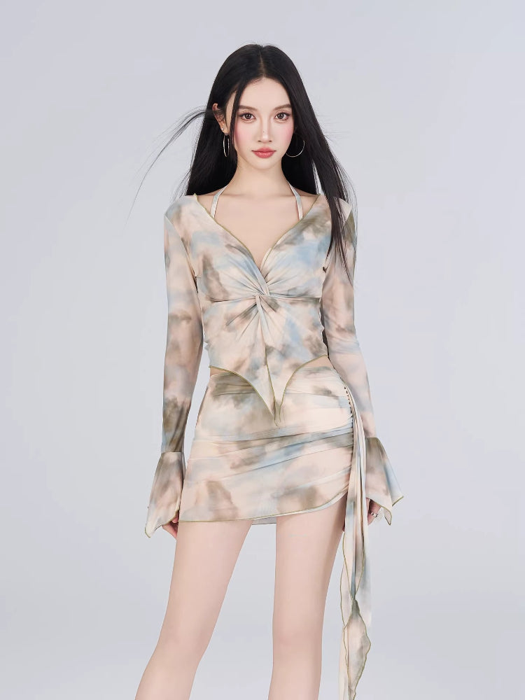 Woman wearing a long-sleeved sheer mesh top with a tie-front detail and a matching abstract print mini skirt.