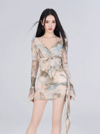 Woman wearing a long-sleeved sheer mesh top with a tie-front detail and a matching abstract print mini skirt.