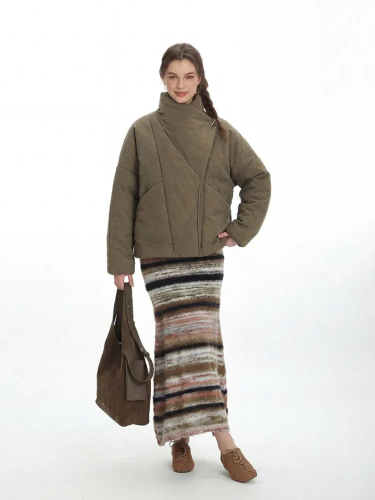 Woman holding a brown tote bag and wearing an olive green quilted jacket and striped maxi skirt.