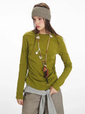 Close-up of a model wearing a long-sleeve olive green top with ruched side detail, grey layered vest, taupe wide-leg pants, yellow handbag, and striped headband.