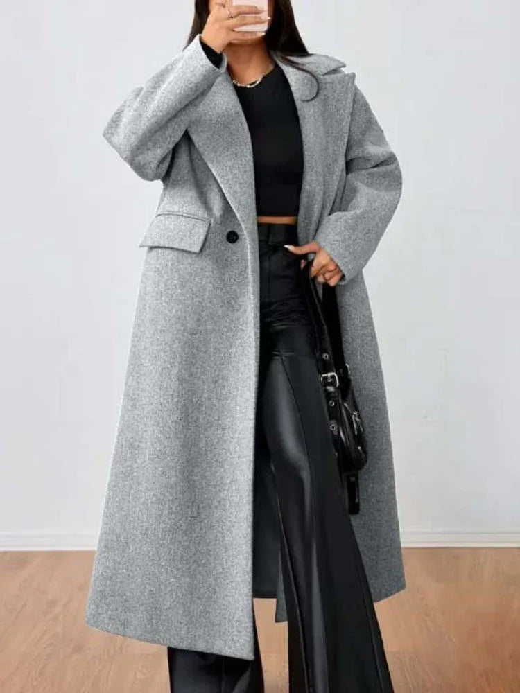 Woman wearing a grey longline wool blend coat with front flap pockets, holding a handbag.