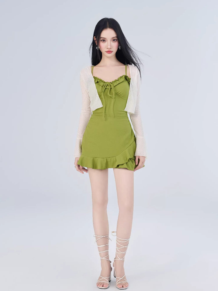 Woman wearing a green textured knit mini dress with ruffled trim and tie-front detail, paired with a white open-knit cardigan with flared sleeves.