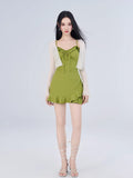 Full body shot of a woman in a green textured knit mini dress with ruffled trim and tie-front detail, and a white open-knit cardigan.