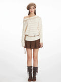 Model wearing a cream-colored off-the-shoulder knit sweater with a diamond pattern and decorative trim. The sweater is paired with a brown textured mini skirt, a decorative belt, brown knee-high socks, and a brown beret.