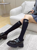 Woman sitting on a couch, showcasing black knee-high socks with a buckle strap and black platform loafers.