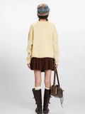 Back view of a woman wearing a yellow knit sweater with a horse graphic print, brown pleated skirt, white socks, and brown boots.