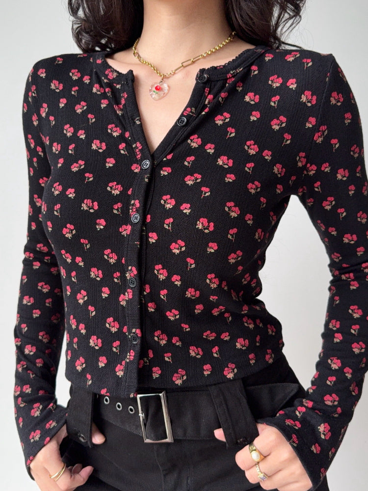 Detail shot of the V-neck and button closure on a black floral print knit top.