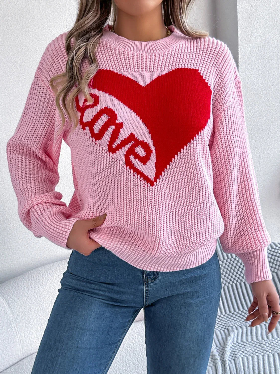 Woman wearing a pink knit sweater with a large red heart graphic and the word 'love' on the front.