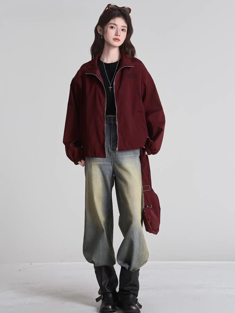 Full body shot of a woman in a maroon bomber jacket and distressed jeans.