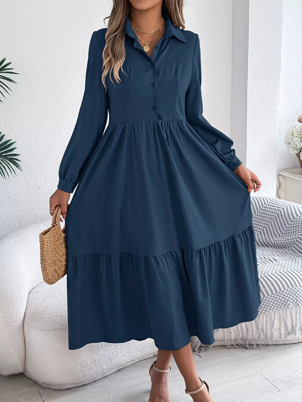 Full-length view of a woman in a navy blue midi dress with a collared neckline and tiered skirt, holding a straw bag.