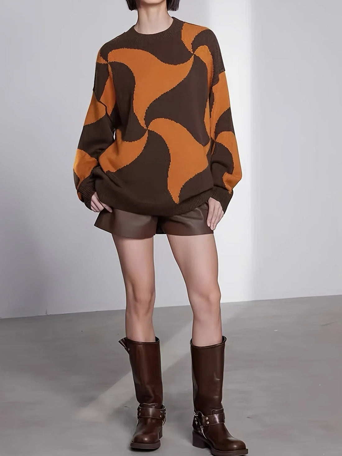Woman wearing a brown and orange abstract patterned knit sweater with brown shorts and knee-high boots.