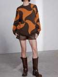 Woman wearing a brown and orange abstract patterned knit sweater with brown shorts and knee-high boots.