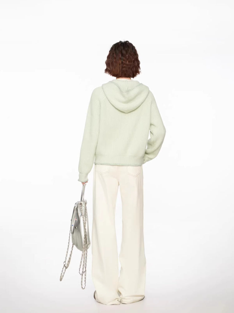 Back view of a woman wearing a light green hooded cardigan with a white top and cream wide-leg pants.