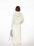 Back view of a woman wearing a light green hooded cardigan with a white top and cream wide-leg pants.