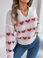 Front view of a woman in a white knit sweater with a red heart pattern.