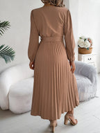 Back view of a woman in a brown long-sleeve V-neck midi dress with a pleated skirt and a self-tie belt
