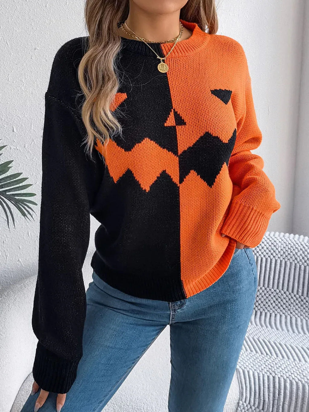 Woman wearing a black and orange two-tone knitted sweater with a jack-o'-lantern graphic on the front.