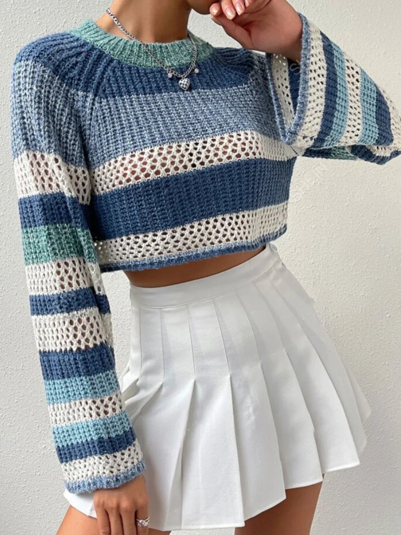 Model posing in a blue, white, and green striped crochet knit cropped sweater with bell sleeves.