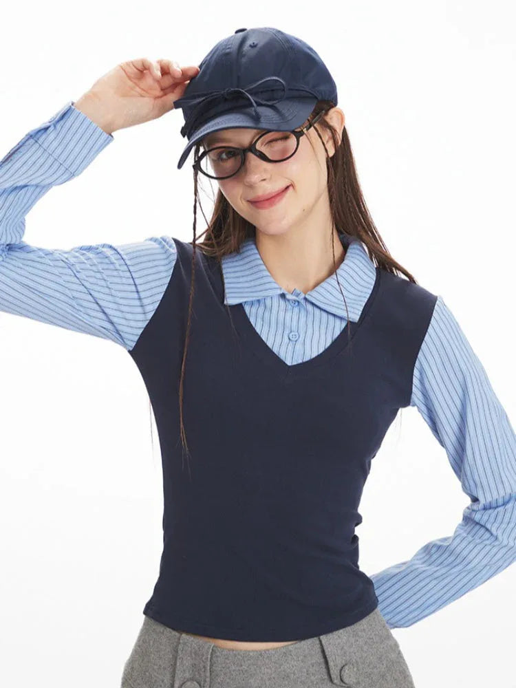 Woman winking and tipping her navy baseball cap, wearing a blue striped collared shirt and navy V-neck vest.
