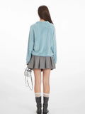 Back view of a model wearing a light blue fuzzy knit long-sleeve collared v-neck sweater with a ribbed hem, paired with a grey pleated mini skirt, grey boots, and a silver handbag.