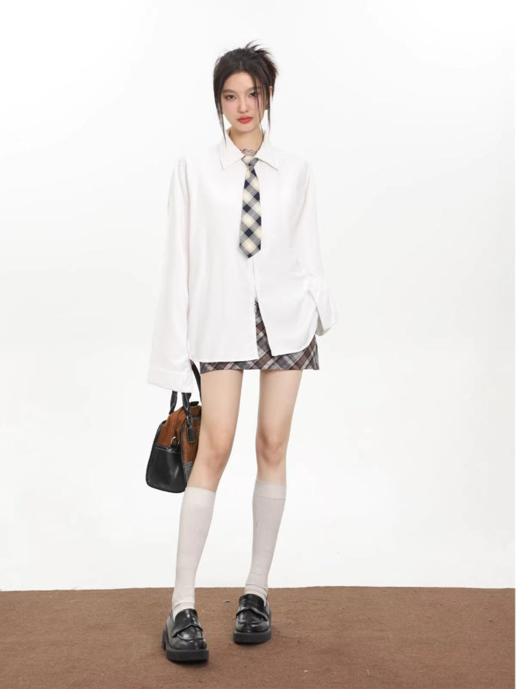 Woman wearing a white oversized collared shirt with a checkered tie, holding a handbag and wearing loafers.
