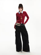Model posing in a red cable knit cardigan layered over a blue collared shirt, paired with black cargo pants.