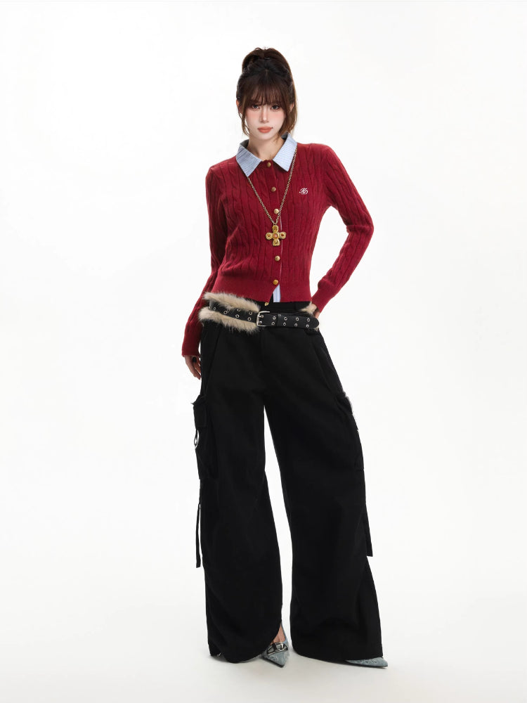 Model posing in a red cable knit cardigan layered over a blue collared shirt, paired with black cargo pants.
