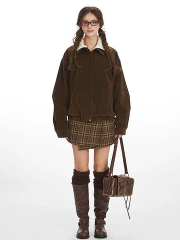 Woman wearing a brown corduroy bomber jacket with a white turtleneck and a plaid skirt.
