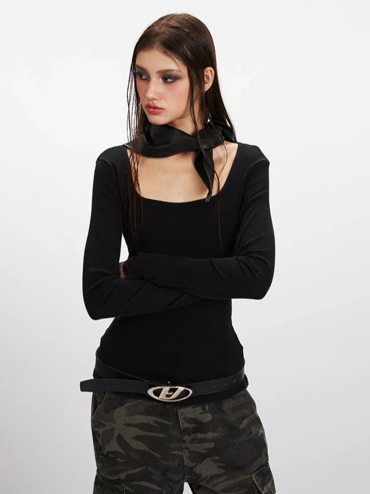 Model posing with arms crossed, wearing a black long-sleeve ribbed top with a square neckline and a detachable scarf, and camouflage cargo pants.