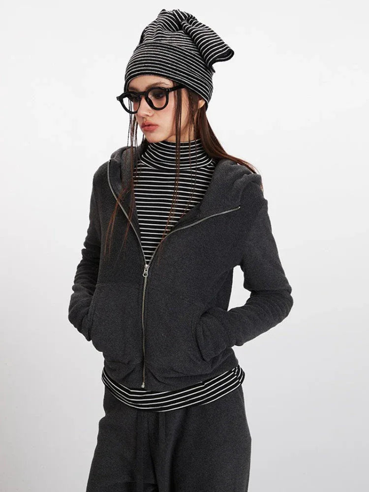 Close-up of a woman wearing a charcoal grey zip-up hooded fleece jacket over a striped turtleneck, with glasses and a beanie.