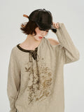 Side view of a woman wearing a beige knit sweater with a graphic print and cold shoulder.
