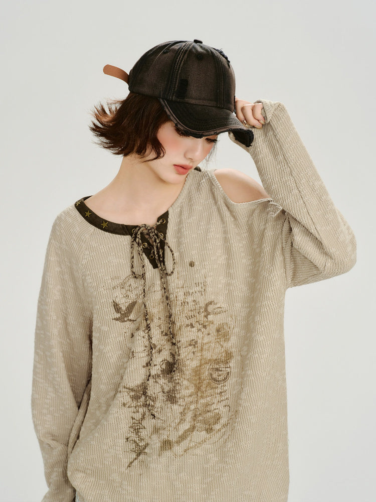 Side view of a woman wearing a beige knit sweater with a graphic print and cold shoulder.