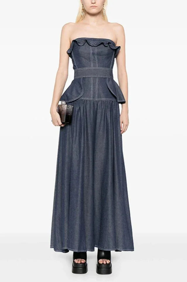 Woman wearing a navy blue denim maxi dress with a ruffled strapless neckline and peplum waist Main image